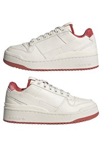 Vita lädersneakers med strukturerad yta, röda detaljer på hälen och en tjock gummisula. Klassisk snörningsdesign med perforeringar.