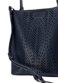 Námořnická kožená kabelka s výřezovým geometrickým vzorem, popruhem přes rameno a hladkou texturou. Obsahuje decentní logo na vrchu.