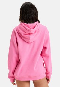 Rosa bomullshoodie med dragsko, avslappnad passform och ribbade ärmslut och nederkant. Baksidan har en slät yta utan mönster.