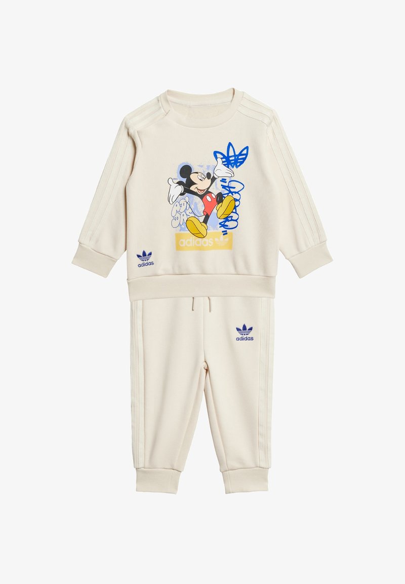 Tuta color crema con grafica di Topolino, dettagli blu, polsini a costine e logo Adidas in viola su parte superiore e pantaloni.