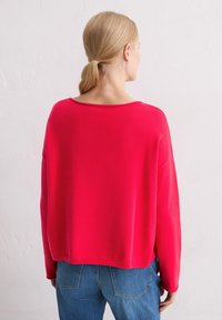Roter, übergroßer Pullover aus einem weichen Stoff, mit weitem Ausschnitt und abgesenkten Schultern, kombiniert mit blauen Jeans.