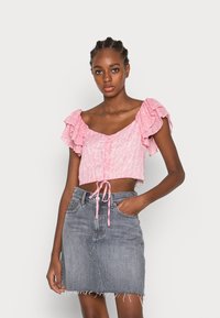 Cropped top cor-de-rosa com mangas com volantes e botões à frente, combinado com uma saia de ganga cinza com bainha desfiada e bolsos laterais.