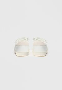 Des baskets blanches montantes avec des cols en peluche et des semelles couleur crème, vues de l'arrière sur un fond blanc uni.