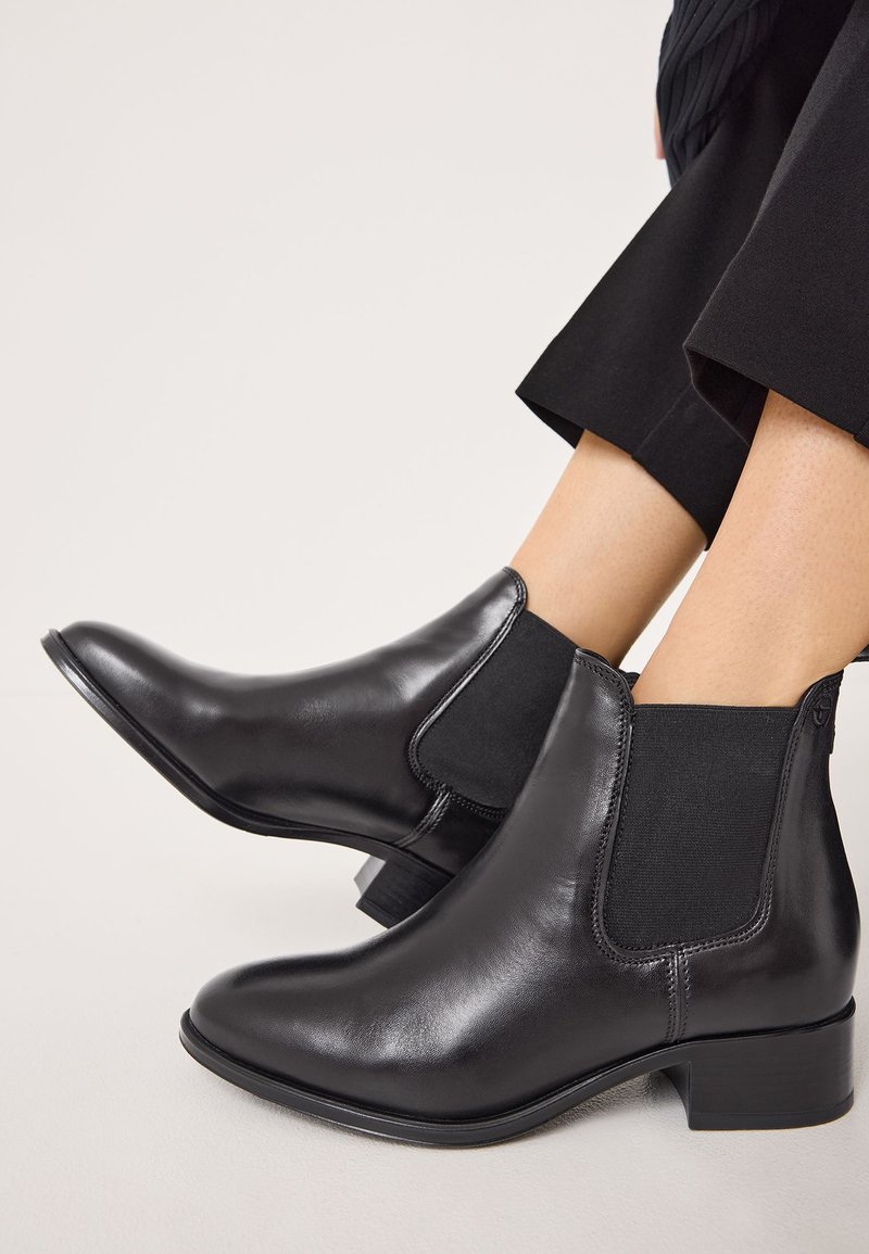 Bottes noires en cuir jusqu'à la cheville avec des panneaux latéraux élastiques, des bouts ronds et des talons bas empilés, arborant une tige lisse et un subtil détail de couture.