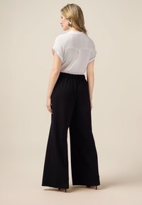 Blouse blanche à manches courtes associée à un pantalon noir à jambes larges, doté d'une taille élastique et d'un léger détail de plis à l'arrière.