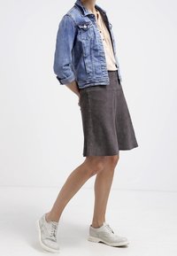 Veste en denim, bleu clair, avec des manches retroussées ; chemise douce couleur sable ; jupe en daim grise ; chaussures gris clair avec un design perforé et un léger compensé.