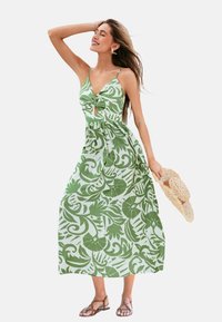 Vestido maxi floral verde con un corsé ajustado, detalle de torsión y ojal. Cuenta con tirantes finos, una falda fluida y un acabado natural.