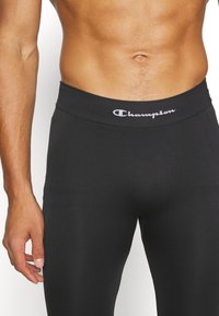 Sorte sorte treningsleggings i svart med en glatt tekstur, elastisk midjebånd med "Champion"-logo i hvitt, og en tettsittende design for aktiv bruk.