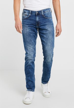 Blue denim jeans with a slim fit, faded detailing, five pockets, and a button fly. Worn with white sneakers.