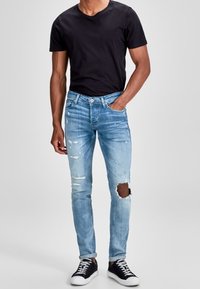 Light blue distressed jeans with ripped details paired with a black t-shirt and black sneakers. Slim fit design with a classic five-pocket style.