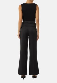 Czarny top bez rękawów zestawiony z czarnymi, szerokimi spodniami. Spodnie mają gładką fakturę i tylne kieszenie. Całość dopełniają buty na obcasie.