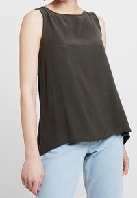 Haut sans manches vert foncé à texture lisse, col rond, coupe ample, associé à un jean bleu clair.