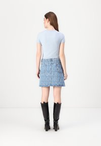 T-shirt fitted azzurro chiaro abbinato a una gonna di jeans leggera a vita alta con un grande motivo a logo e stivali neri fino al ginocchio.