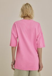Overmaatse roze t-shirt met korte mouwen, een ronde hals en een soepele katoenen textuur, gecombineerd met groene geruite shorts.