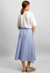 Biała, oversize t-shirt, niebieska spódnica do kolan z elastycznym pasem, noszona z beżowymi, plecionymi sandałami wsuwanymi, lekka tekstura materiału.