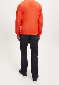 Pomarańczowa bluza z prążkowanymi mankietami i ściągaczem, zestawiona z ciemnymi dżinsami i czarnymi sneakersami. Widok od tyłu. Gładka faktura.