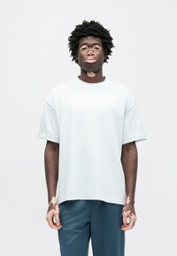 Φαρδιά γαλάζια μπλούζα με γυρισμένα μανίκια, με μικρό λογότυπο στο στήθος. Συνδυασμένη με σκούρο μπλε παντελόνι.