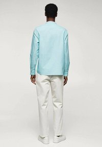 Hellblaues Hemd mit langen Ärmeln und geradem Schnitt, kombiniert mit weißen Hosen und weißen Turnschuhen. Glatter Stoff mit minimalen Details.