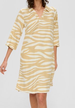 Vrouw draagt een beige en wit zebra-gestreepte jurk tot op de knie met driekwartmouwen en een V-hals.