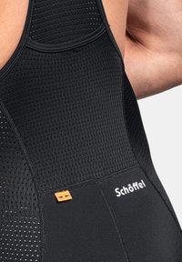 Schwarzes technische Kleidungsstück mit einem strukturierten Mesh-Design, glatten Kanten und einem orangefarbenen Etikett, auf dem der Markenname "Schöffel" deutlich sichtbar ist.