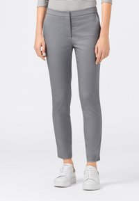 Grå skräddarsydda byxor med en slät yta, rak passform och fotlång fåll, i kombination med vita sneakers. Diskret fickdetaljering.