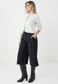 Jasnoszary sweter dzianinowy z okrągłym kołnierzem i guzikami, w połączeniu z czarnymi szerokimi spodniami z wysokim stanem oraz czarnymi butami za kolano.