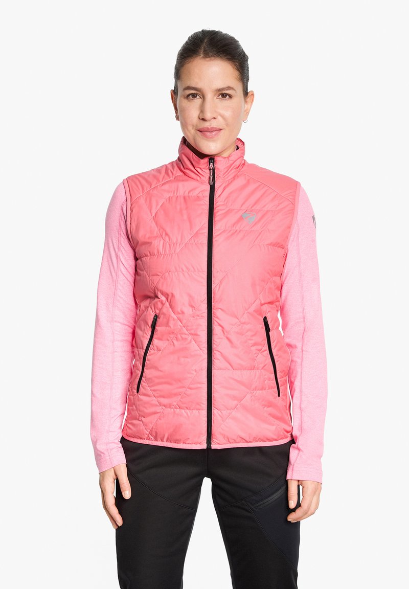 Rosafarbene gesteppte Weste mit Stehkragen, Frontreißverschluss und zwei Seitentaschen, über einem langärmeligen hellrosa Hemd getragen. Schwarze Hose.