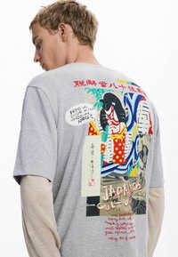 Sivý bavlnený tričko s viacfarebnou japonskou potlačou na chrbte, obsahujúce výrazné grafiky, kanji písmo a červené akcenty.