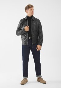 Černá kožená bunda s předním zipem, bočními kapsami a kapsou na hrudi, v kombinaci s tmavě modrými džínami a hnědými botami. Jednoduchý a čistý design.