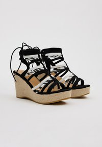 Sandalias de cuña con un diseño de tiras en blanco y negro, fabricadas en ante y tejido, con una suela texturizada estilo espadrille.