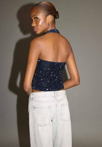 Tmavomodrý flitrový top na krk s priliehavým strihom, skombinovaný s svetlosivými širokými nohavicami s zadnými vreckami a viditeľným šitím.