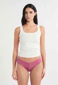 Canotta bianca con scollo quadrato e bottoni frontali, abbinata a una mutandina rosa a vita alta con una larga fascia in vita a contrasto.