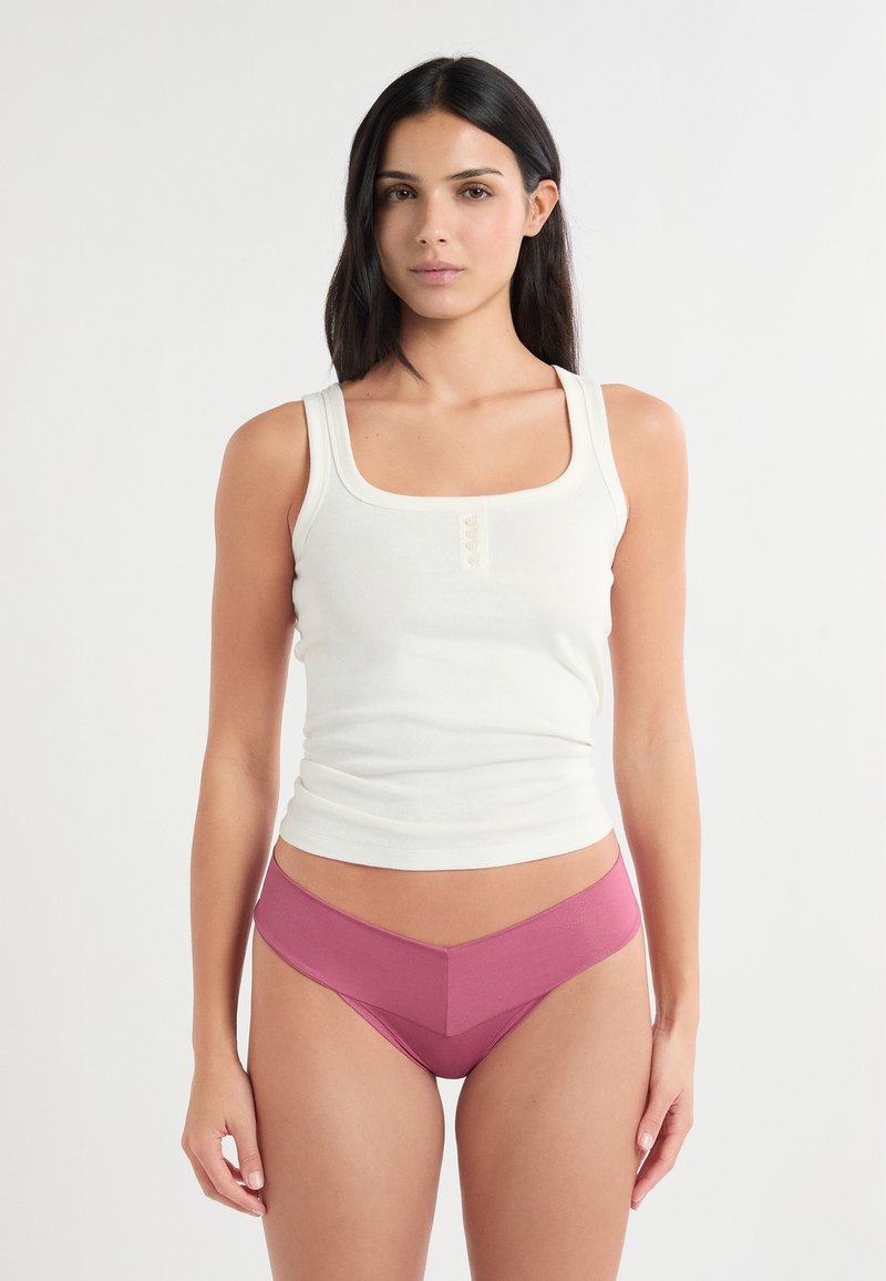 Canotta bianca con scollo quadrato e bottoni frontali, abbinata a una mutandina rosa a vita alta con una larga fascia in vita a contrasto.