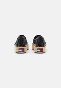 Espadrilles met een zwarte geweven bovenkant met een patroon, een jute touwzool en een merklabel in rood, wit en blauw op de hiel.