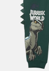 Green sweatshirt featuring a large dinosaur graphic with yellow eye, "Jurassic World" text, and dinosaur spine detailing along the side.