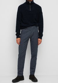 Maglione zip-neck blu navy abbinato a pantaloni grigi a quadri. Il tessuto è in maglia, liscio, con una vestibilità comoda e motivi sottili, completato da stivali neri.