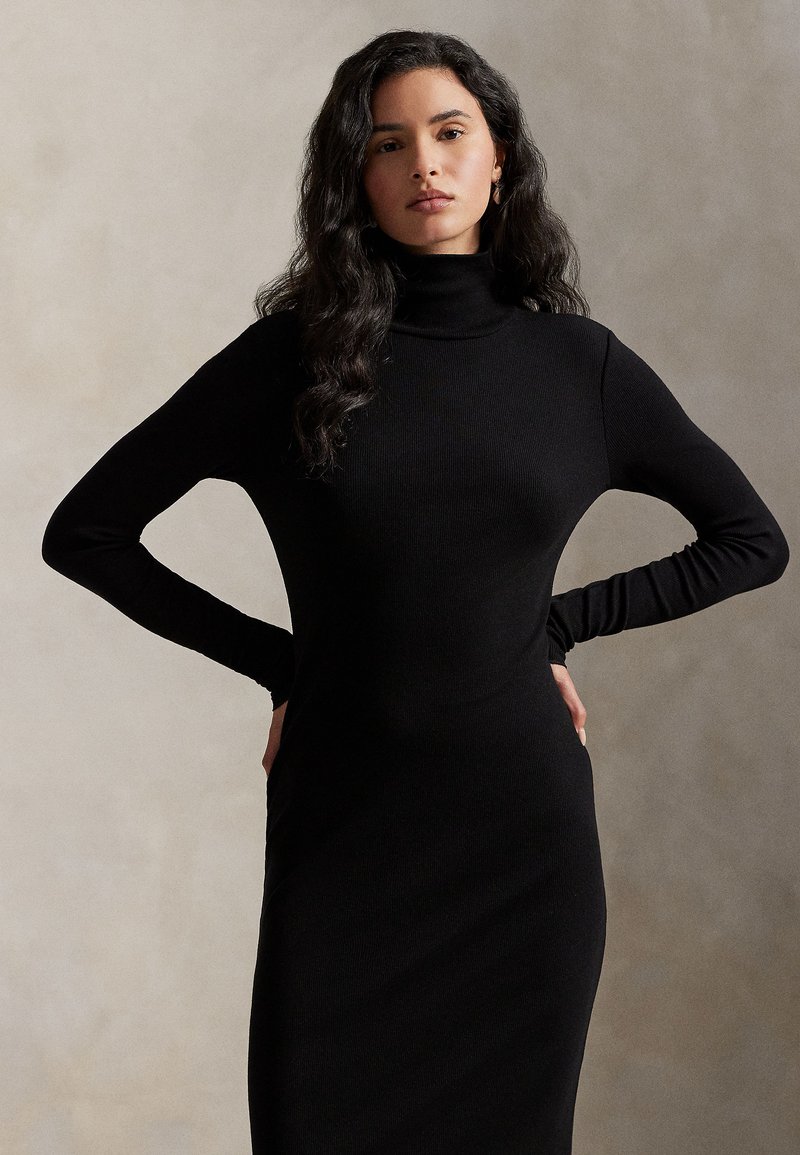 Μαύρο ριγωτό φόρεμα με ζιβάγκο, μακρυά μανίκια, εφαρμοστή γραμμή και λεία υφή, παρουσιάζεται πάνω σε ουδέτερο φόντο.