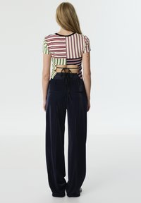Multicolored gestreepte crop top met korte mouwen en uitsnijding aan de achterkant, gecombineerd met losse marineblauwe broek.