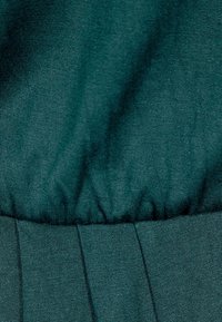 Gros plan d'un tissu vert foncé montrant une couture élastique froncée et des détails de tissage texturé.