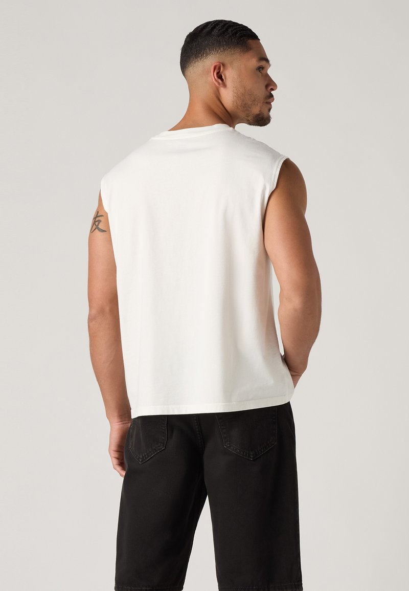 Weißes ärmelloses Baumwolloberteil in lockerer Passform mit Rundhalsausschnitt und glatter Textur, kombiniert mit schwarzen Cargo-Shorts.