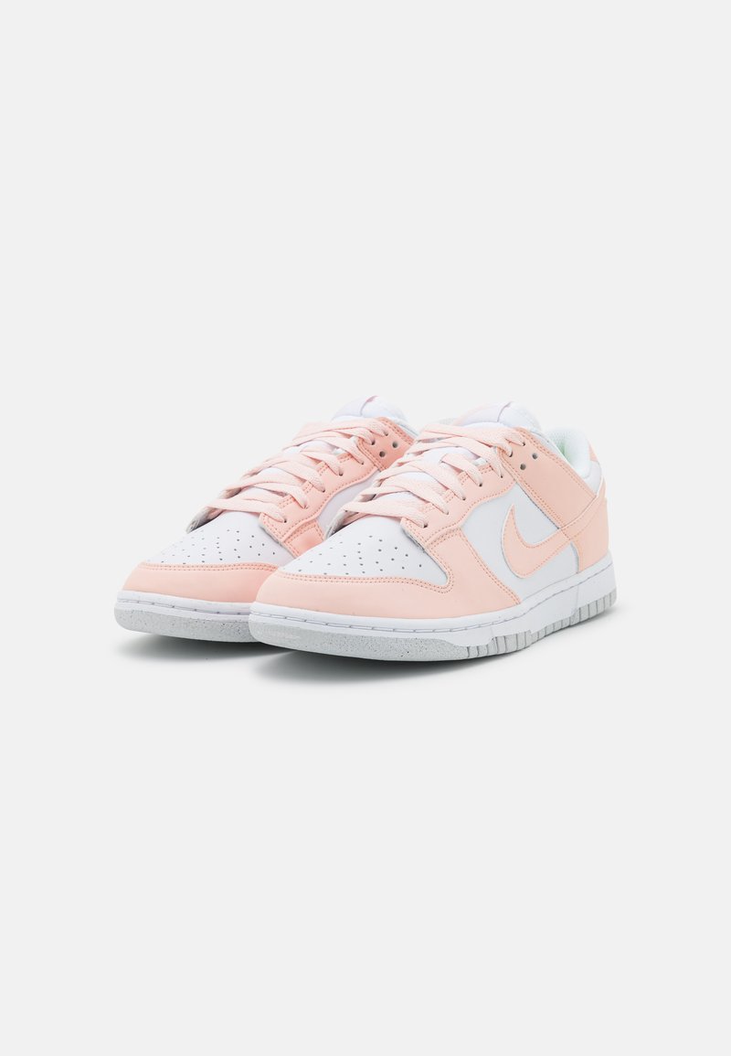 Nike Sneakers in einer Farbgestaltung aus Weiß und Zartrosa, mit einem oberen Teil aus glattem Leder, einer perforierten Zehenbox und einer strukturierten weißen Gummisohle.