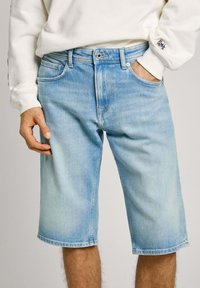 Shorts de mezclilla azul claro con corte recto, que incluyen bolsillos frontales, presillas para el cinturón y un acabado desgastado. Dobladillo cosido a la altura de las rodillas.