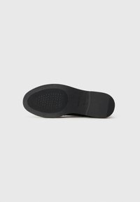 Black rubber shoe sole with textured grip pattern and slight arch. Smooth edges; minimal branding visible on heel area.