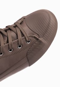 Zapatilla de cuero marrón con una puntera texturizada y estriada, cordones planos y ojales de metal. Cuerpo liso con una suela flexible.