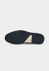Semelle de chaussure avec un motif de grip texturé noir et un insert de support triangulaire beige sur un fond clair uni.