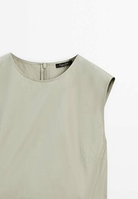 Blouse sans manches de couleur beige clair avec un col rond et une fermeture éclair au dos, à plat sur un fond blanc.