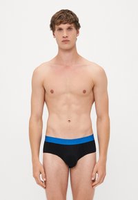 Zwarte slips met een blauwe elastische tailleband met "HUGO" branding. De stof lijkt zacht, en het ontwerp is klassiek en aansluitend.