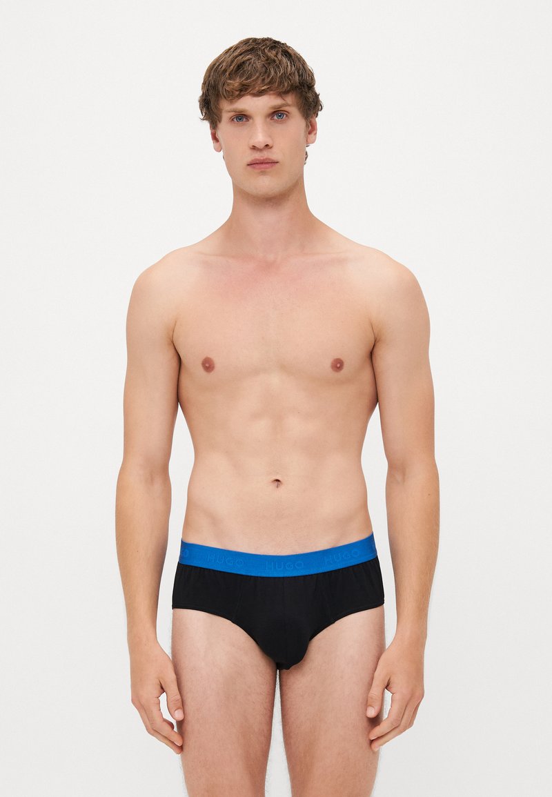 Zwarte slips met een blauwe elastische tailleband met "HUGO" branding. De stof lijkt zacht, en het ontwerp is klassiek en aansluitend.