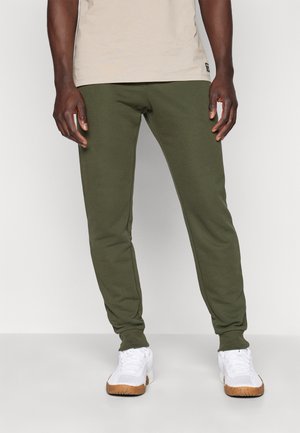 Pantaloni de trening din bumbac de culoare verde măsliniu, cu croială conică, talie cu bandă elastică și buzunare laterale, asortați cu adidași albi cu talpă din cauciuc.