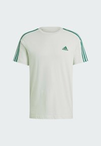 Maglietta verde chiaro in cotone, con collo rotondo, maniche corte e tre strisce verde scuro su ciascun spallaccio. Piccolo logo sul petto.